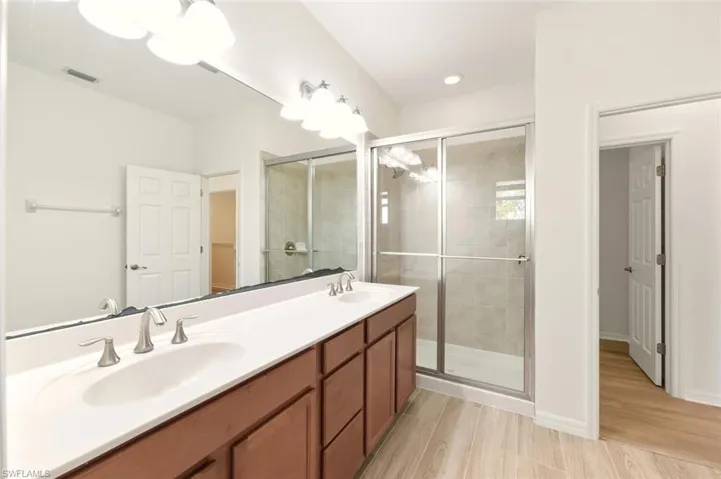 Bathroom with double vanity, a stall shower, and light wood finished floors