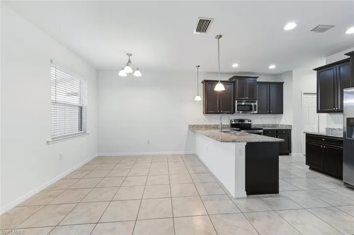 Kitchen with a peninsula, appliances with stainless steel finishes, pendant lighting, light stone counters, and a chandelier