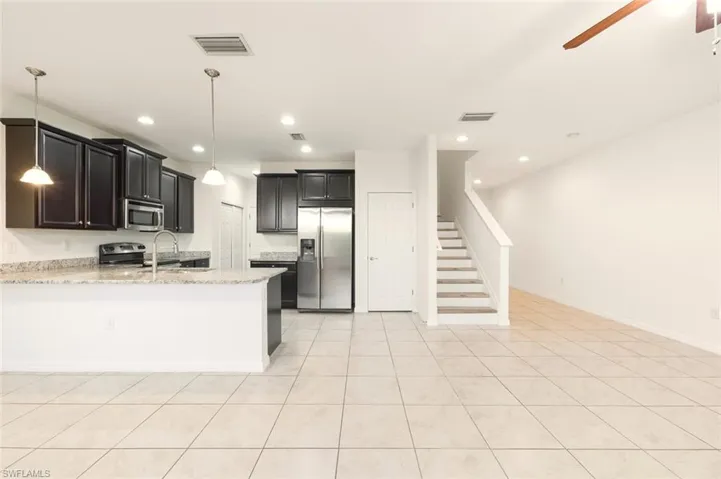 Kitchen featuring appliances with stainless steel finishes, light stone countertops, a peninsula, dark cabinetry, and hanging light fixtures