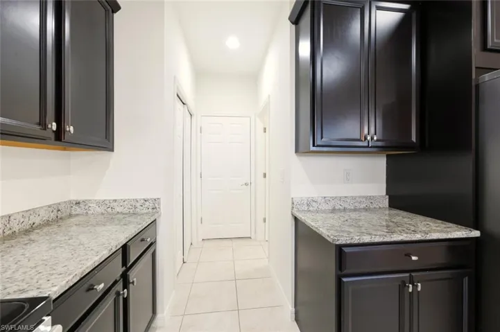 Kitchen featuring light stone countertops, range with electric cooktop, light tile patterned floors, and freestanding refrigerator