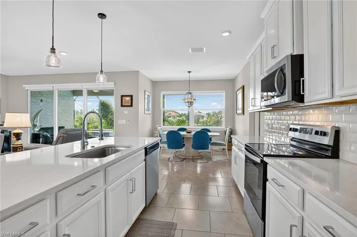Kitchen featuring stainless steel appliances, white cabinetry, decorative light fixtures, light stone countertops, and light tile patterned floors