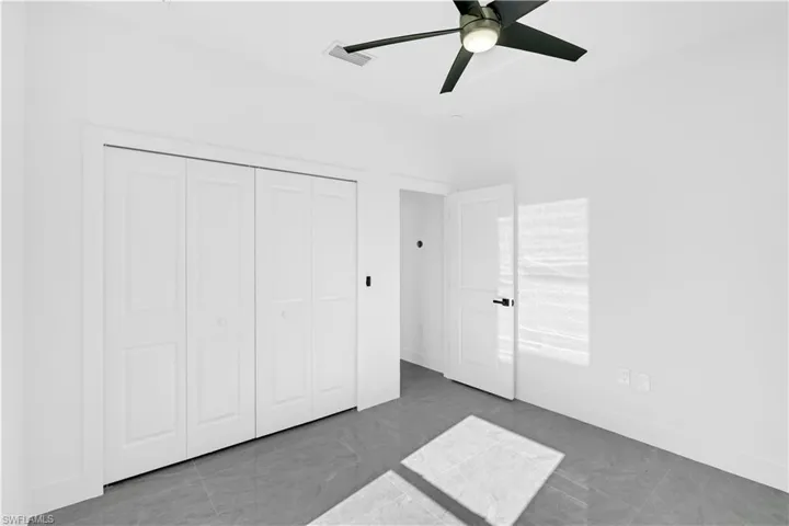 Bright room featuring white walls, gray tile flooring, a modern ceiling fan with integrated lighting, and white bi-fold closet doors