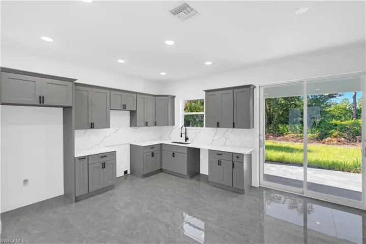 Kitchen featuring grey shaker-style cabinetry, white countertops with veining, a white backsplash, and a matte black faucet