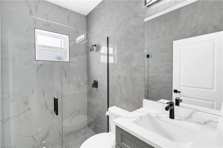 Modern guest bathroom featuring a walk-in shower with clear glass enclosure, large format stone-look wall tiles, and a window