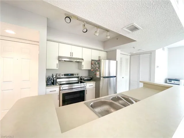 Kitchen featuring stainless steel appliances, a textured ceiling, light countertops, white cabinetry, and rail lighting