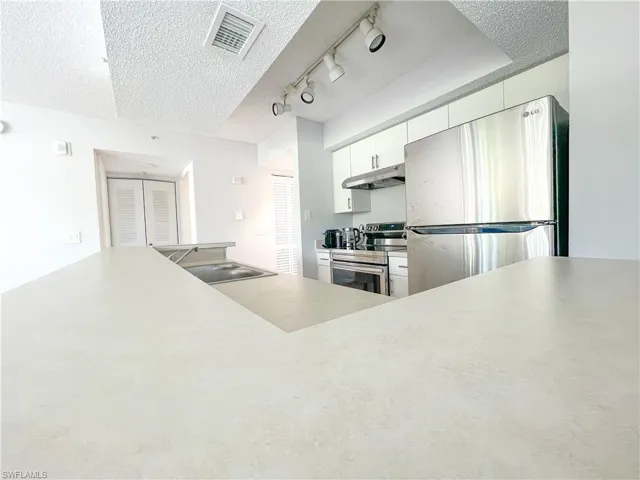 Kitchen with a textured ceiling, appliances with stainless steel finishes, light countertops, white cabinets, and under cabinet range hood