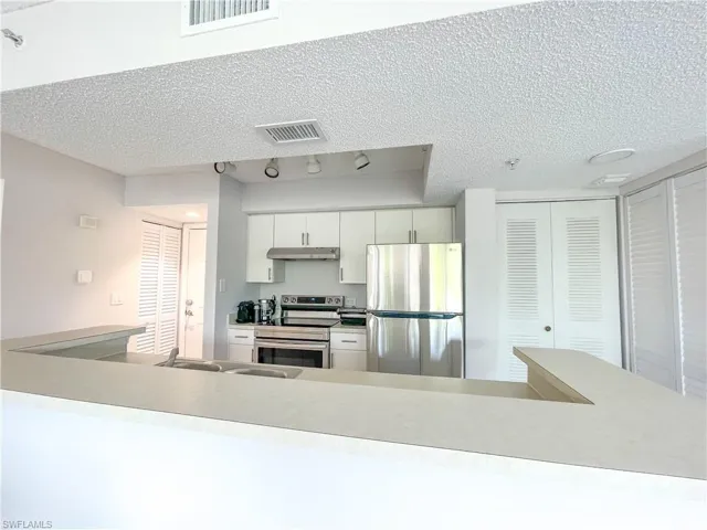 Kitchen with appliances with stainless steel finishes, light countertops, a textured ceiling, under cabinet range hood, and white cabinetry