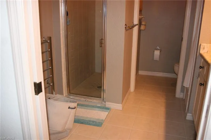 Full bathroom with vanity, a stall shower, light tile patterned floors, a textured wall, and a towel warming rack