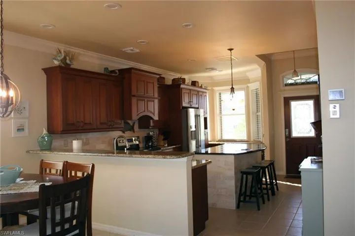 Kitchen with a peninsula, a kitchen breakfast bar, stainless steel appliances, light tile patterned floors, and crown molding