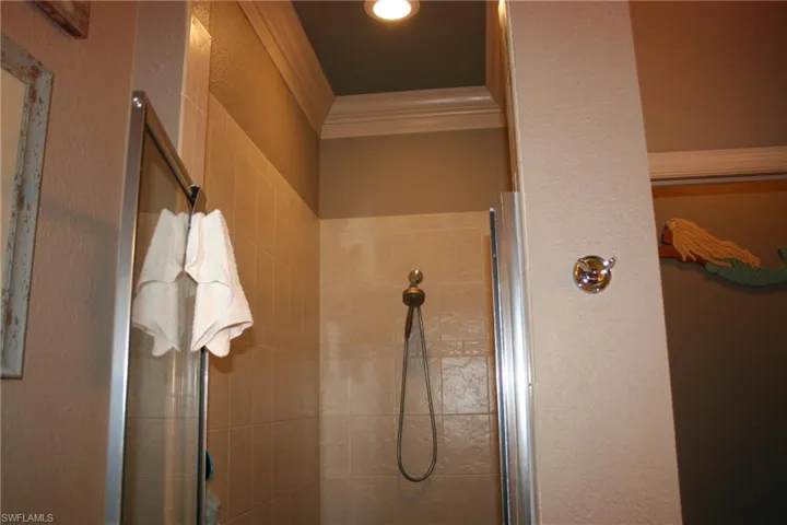 Bathroom with a textured wall, crown molding, and a shower stall