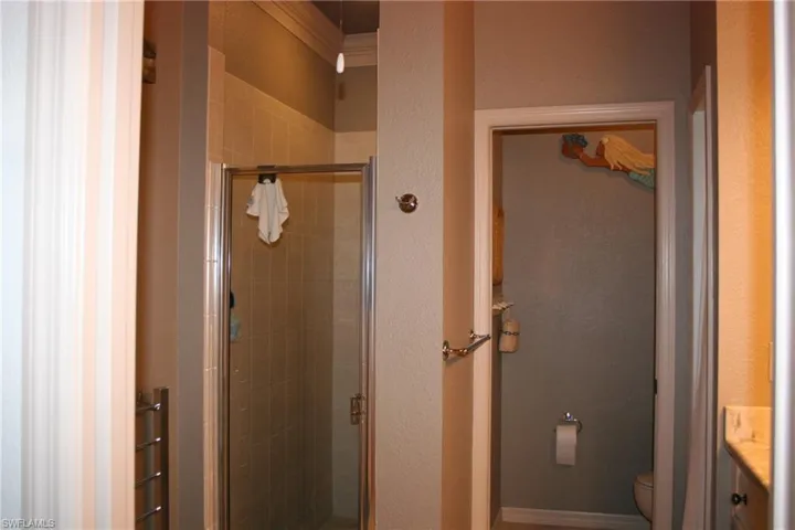 Full bathroom with vanity, a stall shower, a textured wall, a towel warming rack, and crown molding
