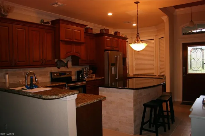 Kitchen featuring a breakfast bar, stainless steel appliances, ornamental molding, hanging light fixtures, and dark stone counters