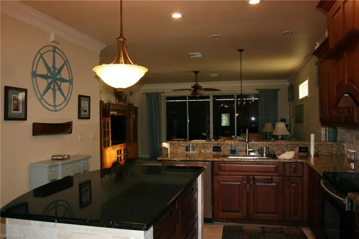 Kitchen featuring dark stone countertops, ornamental molding, a center island, decorative light fixtures, and a peninsula