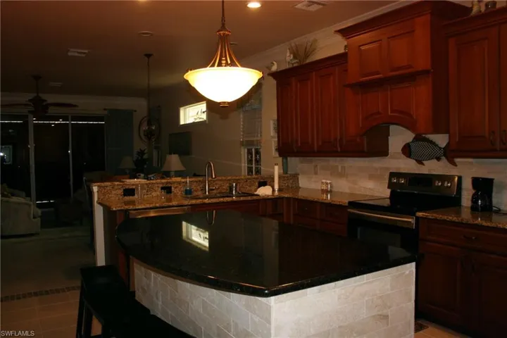 Kitchen with range with electric stovetop, dark stone counters, a kitchen breakfast bar, a peninsula, and backsplash