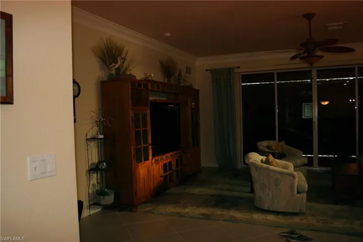 Living area with ceiling fan, dark tile patterned flooring, and ornamental molding