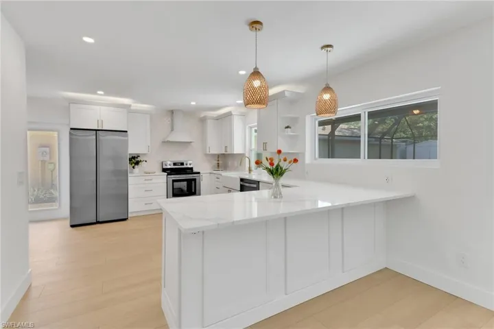 Kitchen featuring appliances with stainless steel finishes, white cabinets, kitchen peninsula, and wall chimney exhaust hood