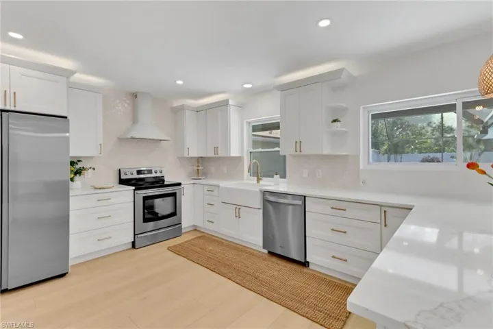 Kitchen featuring wall chimney range hood, light wood-type flooring, stainless steel appliances, backsplash, and sink