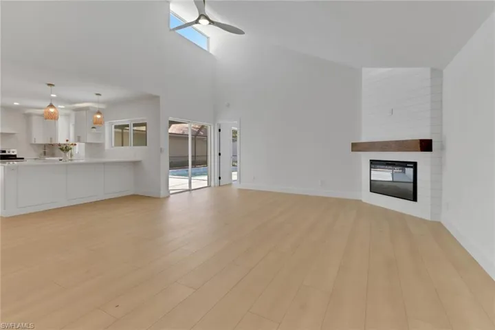 Unfurnished living room with light hardwood / wood-style floors, a fireplace, a towering ceiling, and ceiling fan