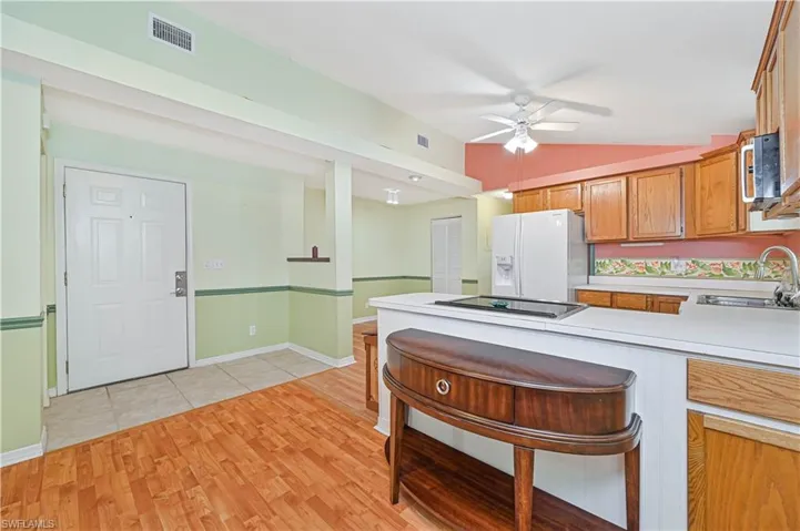 Kitchen featuring cooktop, white fridge with ice dispenser, sink, ceiling fan, and light hardwood / wood-style flooring