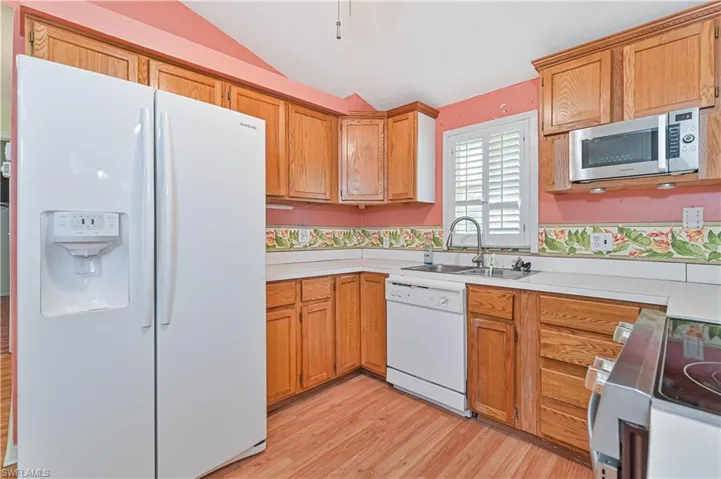 Kitchen featuring light hardwood / wood-style floors, sink, white appliances, and vaulted ceiling