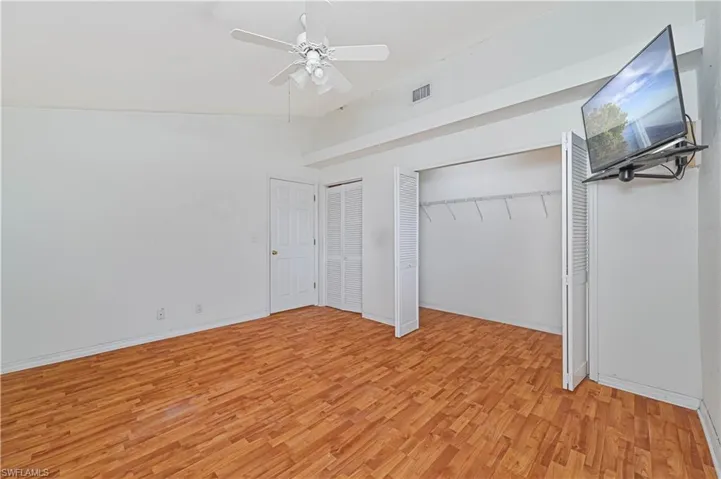 Unfurnished bedroom featuring multiple closets, light hardwood / wood-style floors, lofted ceiling, and ceiling fan