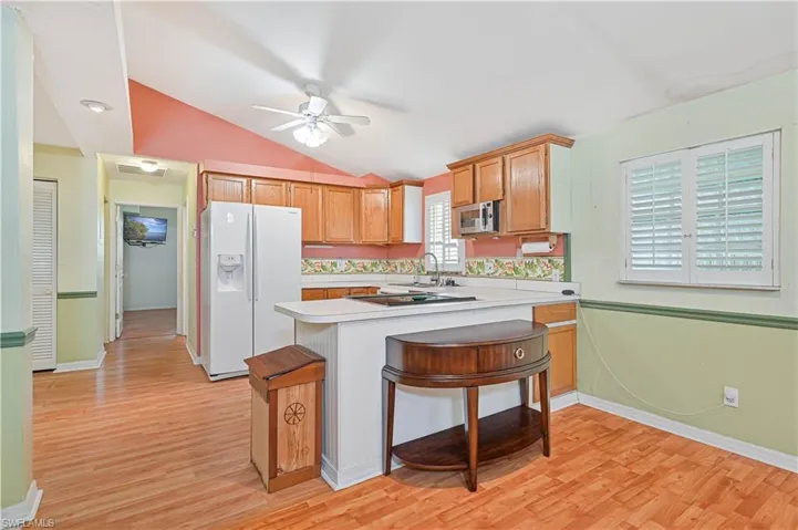 Kitchen with a breakfast bar, kitchen peninsula, white refrigerator with ice dispenser, light hardwood / wood-style flooring, and vaulted ceiling