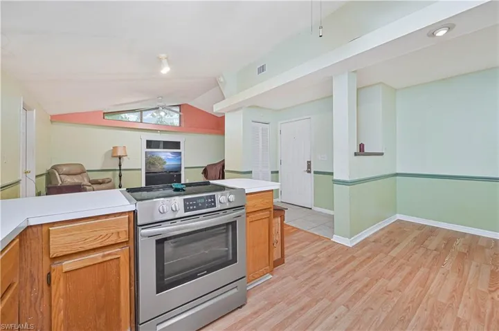Kitchen featuring kitchen peninsula, ceiling fan, stainless steel range with electric stovetop, light wood-type flooring, and vaulted ceiling