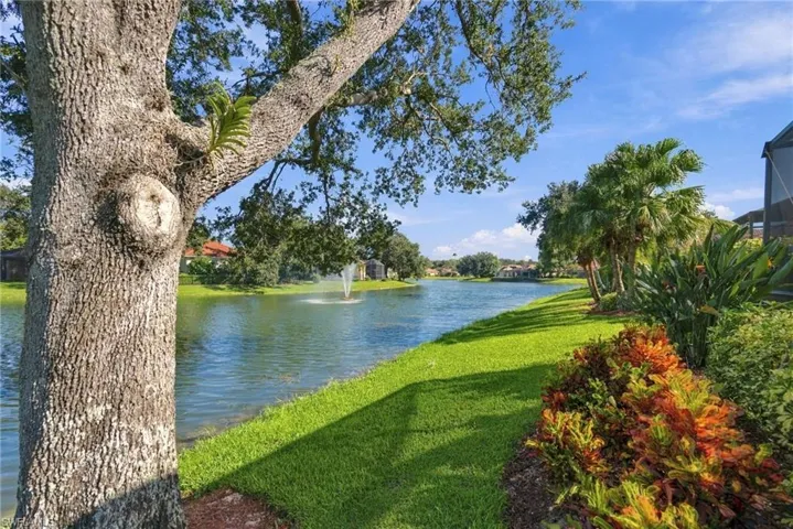 Waterfront parcel featuring a manicured lawn, mature trees, ornamental foliage, and a decorative water fountain