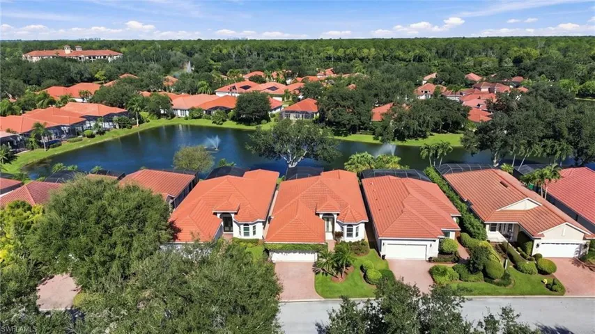 Aerial perspective of residential properties featuring clay tile roofing, paved driveways, mature landscaping, and water frontage
