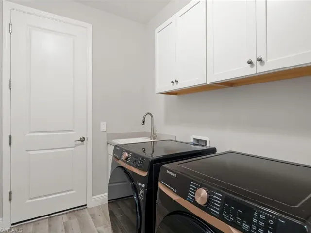 Laundry room featuring washing machine and dryer, cabinet with laundry tub and light wood-style floors