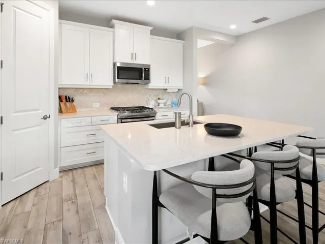 Kitchen featuring herringbone backsplash, light wood-type flooring, appliances with stainless steel finishes, a center island with sink, and a kitchen breakfast bar