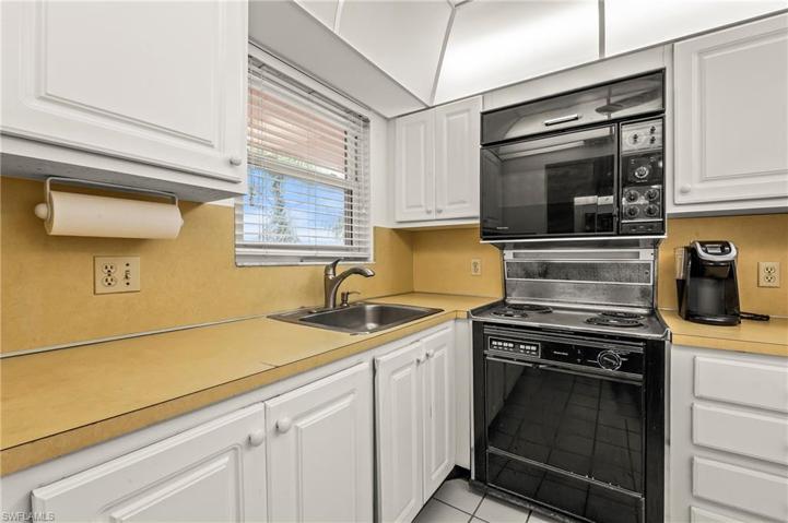 The roomy kitchen features tile floors, white cabinetry and a hurricane impact window.