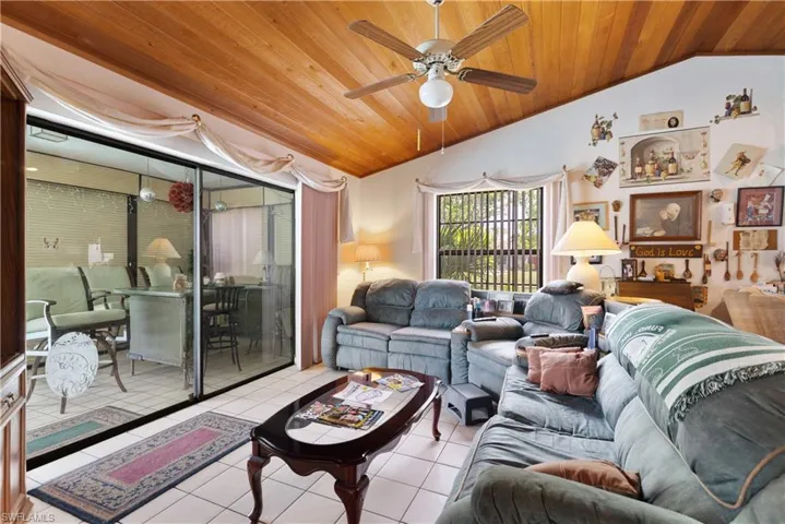 Living room with lofted ceiling, wood ceiling, light tile patterned flooring, and a ceiling fan