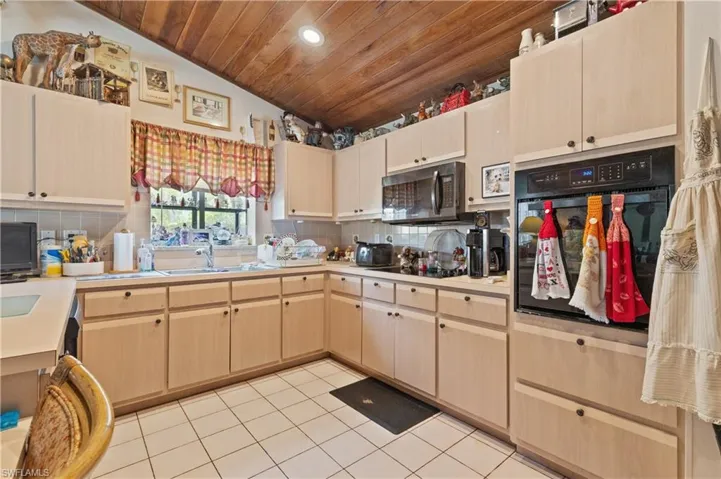 Kitchen featuring black appliances, wood ceiling, light brown cabinets, light tile patterned flooring, and light countertops