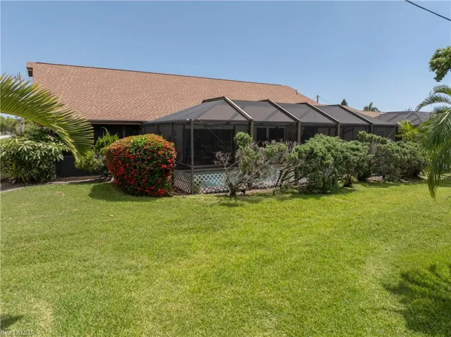 Rear view of house with a lawn, a shingled roof, and glass enclosure