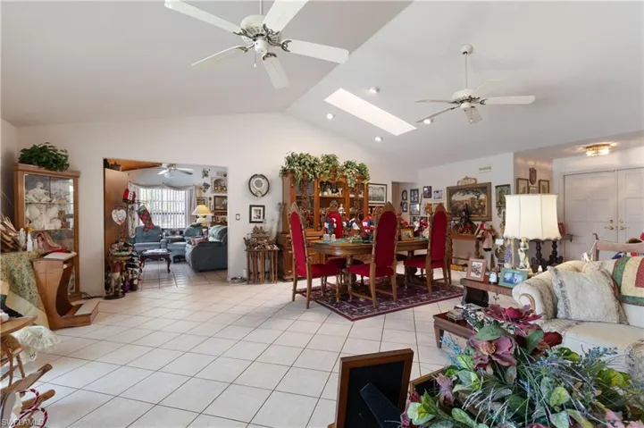 Living room featuring vaulted ceiling, light tile patterned flooring, a ceiling fan, and a skylight