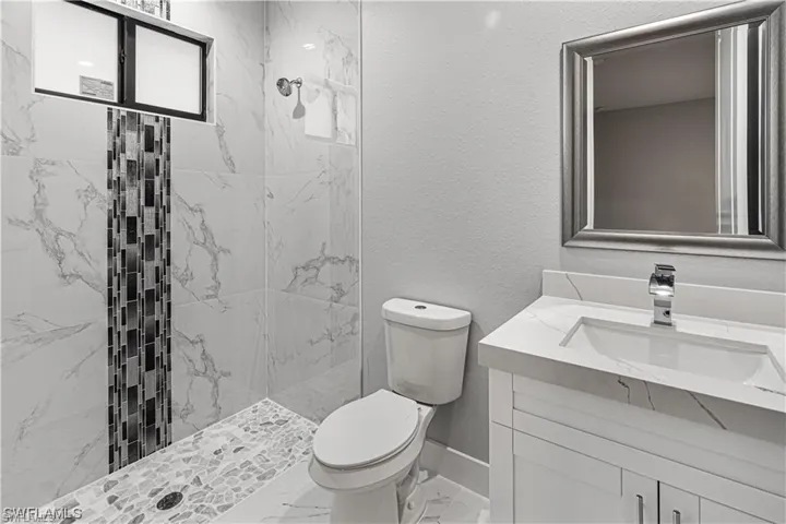 Bathroom with tiled shower, vanity, and toilet