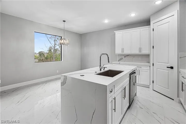 Kitchen with a center island with sink, white cabinetry, an inviting chandelier, and light stone counters