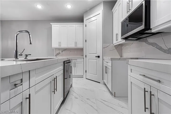 Kitchen with decorative backsplash, stainless steel appliances, white cabinets, and sink