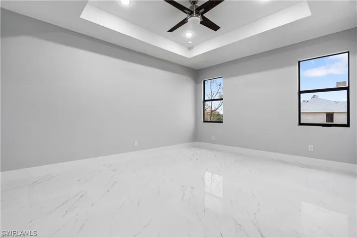 Unfurnished room featuring a tray ceiling, ceiling fan, and a healthy amount of sunlight