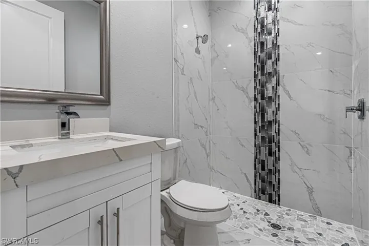 Bathroom with toilet, vanity, and tiled shower