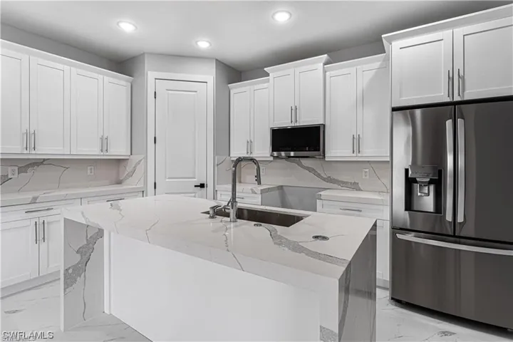 Kitchen featuring stainless steel fridge, white cabinetry, sink, and an island with sink