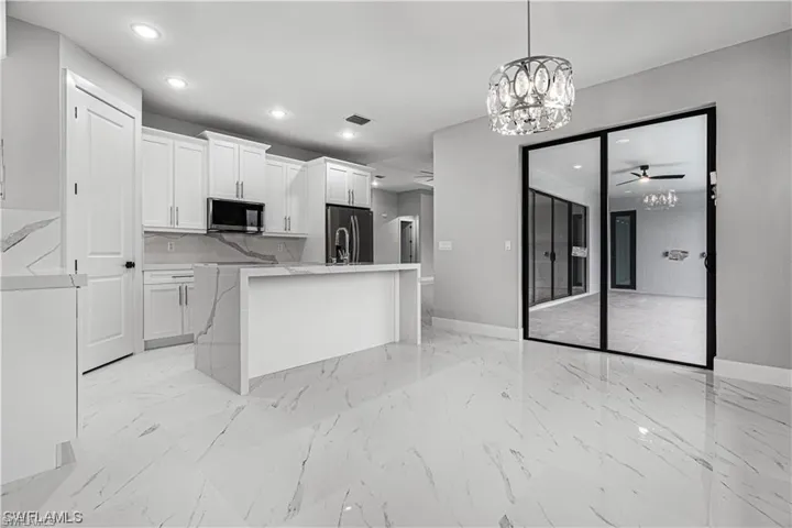 Kitchen with ceiling fan with notable chandelier, white cabinets, hanging light fixtures, a center island with sink, and appliances with stainless steel finishes