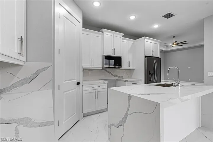 Kitchen featuring light stone counters, sink, white cabinetry, stainless steel appliances, and ceiling fan