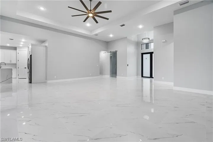 Unfurnished living room featuring a barn door, a raised ceiling, a high ceiling, and ceiling fan