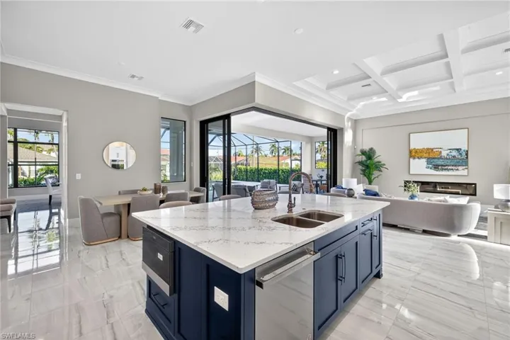 Kitchen featuring open floor plan, light stone countertops, blue cabinets, dishwasher, and a kitchen island with sink