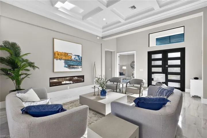 Living room with a high ceiling, coffered ceiling, beam ceiling, marble tiled flooring, and a glass covered fireplace