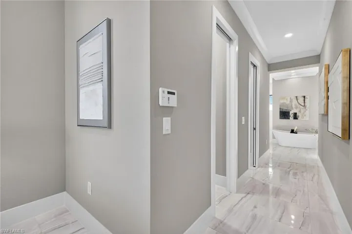 Corridor with light marble finish floors, ornamental molding, and recessed lighting