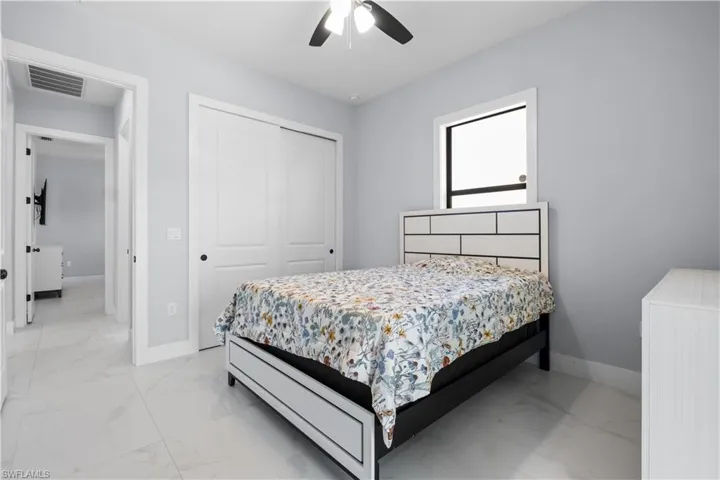 Well-lit room featuring tile flooring, a window with black trim, a ceiling fan, and white sliding closet doors
