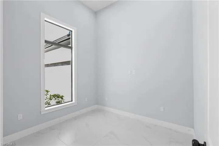 Room featuring a tall vertical window with white trim, light gray painted walls, and large format white tile flooring
